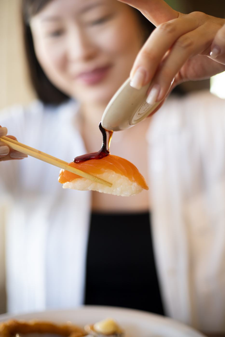 Nigiri de salmão recebendo shoyu, segurado no hashi